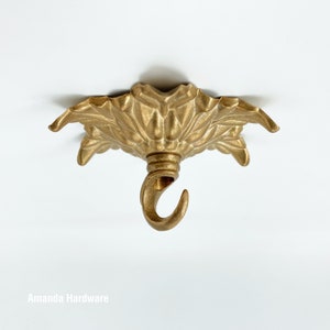 May include: Gold metal ceiling canopy with a decorative floral design and a hook for hanging a light fixture.