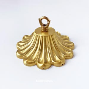 May include: Gold metal ceiling canopy with a scalloped edge and a decorative ring for hanging a light fixture.