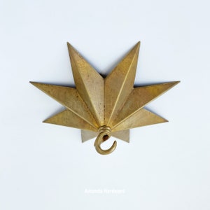 May include: A gold-toned metal starburst ceiling fixture with a hook for hanging a light fixture. The starburst has eight points and is made of a textured metal.