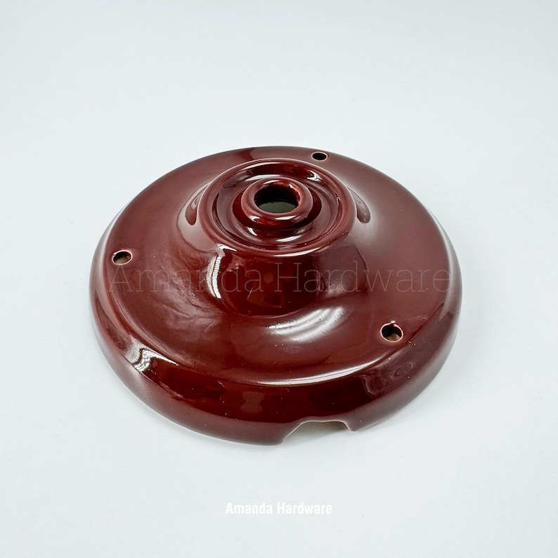 May include: A maroon-colored ceramic ceiling canopy with a glossy finish. The canopy has a central hole and several smaller holes around the perimeter. The text "Amanda Hardware" is printed at the bottom.