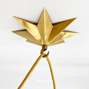 Può includere: Un apparecchio di illuminazione a soffitto a forma di stella dorata con un gancio per appendere un apparecchio di illuminazione. L'apparecchio è in metallo e ha una finitura lucida.