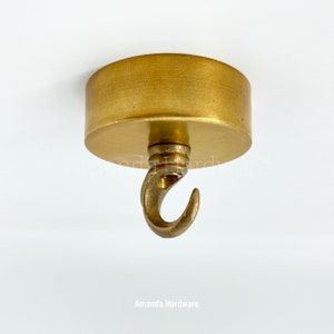 May include: A gold ceiling hook with a round base and a curved hook. The hook is made of metal and has a polished finish.