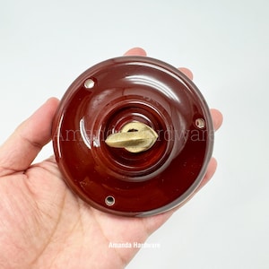 May include: A round, dark brown ceramic door knob with a brass-colored handle. The knob has a glossy finish and three small holes around the edge. The text "Amanda Hardware" is visible at the bottom.
