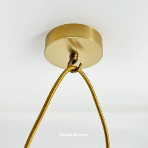 May include: A gold ceiling mount with a hook for hanging a light fixture. A gold cord is attached to the hook.