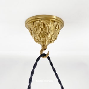 May include: A gold ceiling fixture with an ornate design and a black electrical cord hanging from a hook.
