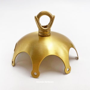 Puede incluir: Un dosel de techo de metal dorado con un anillo decorativo en la parte superior. El dosel tiene cuatro bordes curvos y un acabado liso.