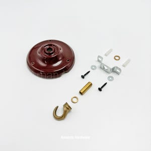 May include: A ceiling hook kit with a maroon-colored circular base, a brass hook, and various hardware components. Includes screws, a metal bracket, and a brass-colored threaded rod. The text "Amanda Hardware" is visible.