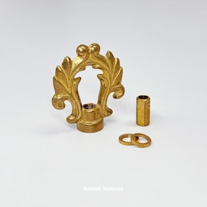 May include: A gold-colored, ornate curtain rod finial with a leaf design, along with a matching threaded sleeve and two rings. The finial has a detailed, vintage aesthetic. The text "Amanda Hardware" is at the bottom.