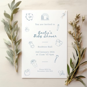 May include: A white rectangular baby shower invitation card with blue line art illustrations of baby items including a piggy bank, rainbow, rattle, diaper, onesie, bib, and pacifier. The text reads: You are invited to Amelia's Baby Shower, Rushton Hall, 2nd January 2026 at 11am 'til 4pm, Please RSVP by November 29th 2025.