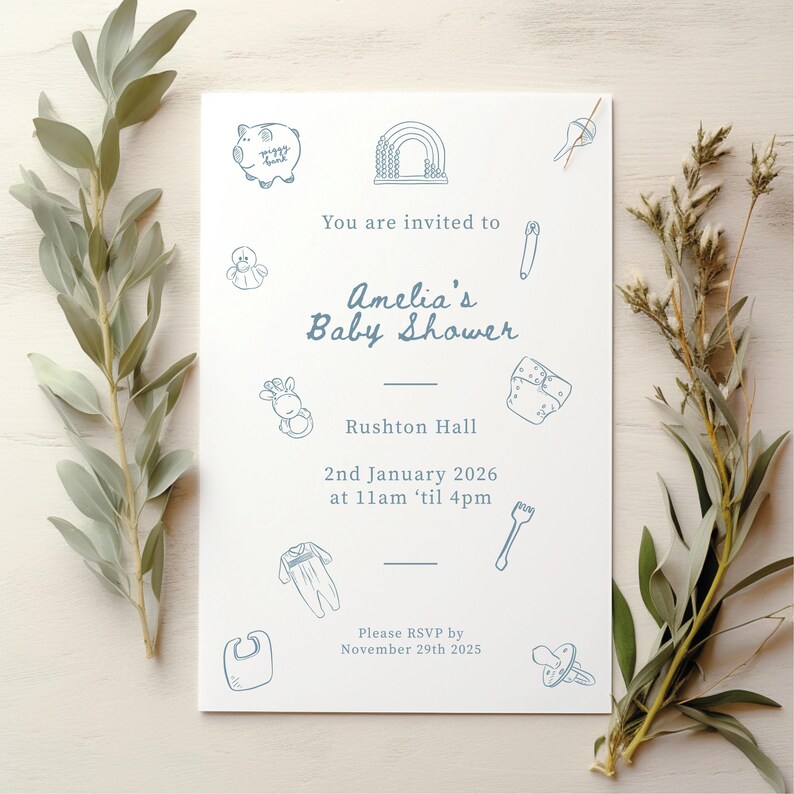 May include: A white rectangular baby shower invitation card with blue line art illustrations of baby items including a piggy bank, rainbow, rattle, diaper, onesie, bib, and pacifier. The text reads: You are invited to Amelia's Baby Shower, Rushton Hall, 2nd January 2026 at 11am 'til 4pm, Please RSVP by November 29th 2025.