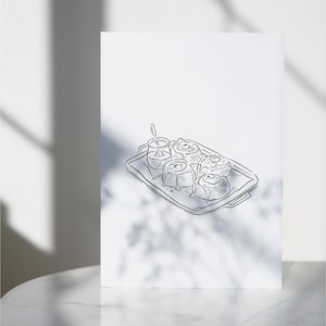 A black and white line drawing of a tray of cinnamon rolls with a small dish of icing on the side.