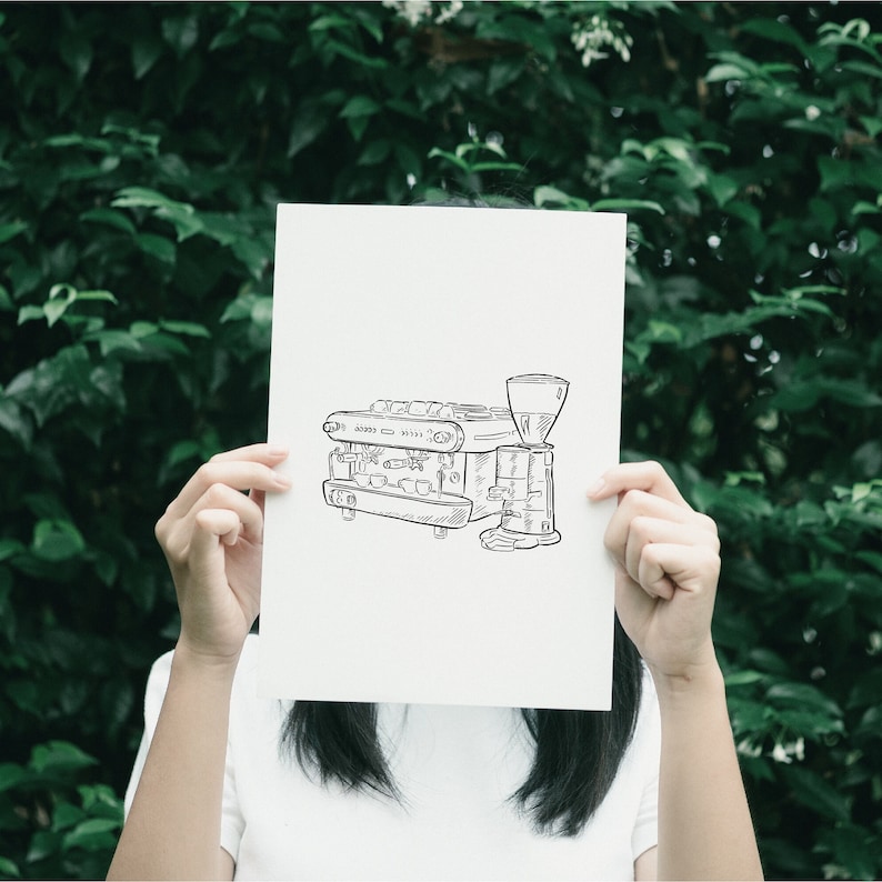 A black and white line drawing of a coffee machine on a white piece of paper held by a person.