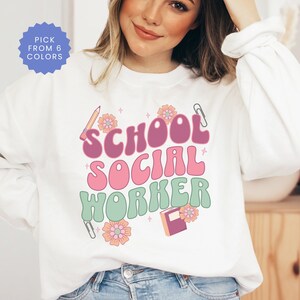May include: White sweatshirt with a pink, green, and purple graphic that says "School Social Worker" with a pencil, book, and paper clips.