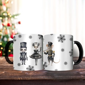 May include: A white ceramic mug with a black handle. The mug features a black and white illustration of a girl, a boy, and a mouse dressed in holiday attire. The background is white with black snowflakes.