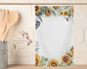 May include: White kitchen towel with a border of watercolor sunflowers, leaves, and stems. The towel has a textured waffle weave. The text "Floral Delights Co. Blooming Warm" is in a circle at the bottom left corner of the towel.