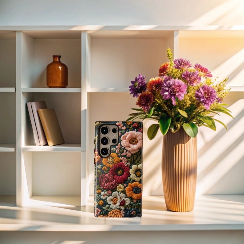 Puede incluir: Una funda de tel&eacute;fono floral con fondo oscuro y una variedad de flores coloridas. La funda tiene una protuberancia de c&aacute;mara elevada con tres lentes.