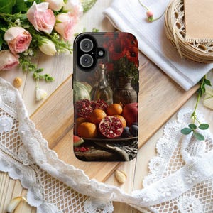 Könnte beinhalten: Eine Handyhülle mit einem Stillleben von Früchten, darunter Granatäpfel, Orangen und Pflaumen, mit einer Flasche und einer Vase. Die Hülle hat einen dunklen Hintergrund mit einem Blumenarrangement. Die Hülle liegt auf einer Holzoberfläche mit Spitze und Blumen.
