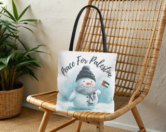 May include: White tote bag featuring a watercolor snowman wearing a black hat and scarf, holding a Palestinian flag. The words "Peace For Palestine" are written in a script font. The bag has black handles.