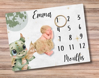 May include: A baby milestone blanket with a green dragon and moon design. The blanket has a white background with gold stars and a rope circle with numbers 1-12 for each month. The text "Emma" and "Months" are printed on the blanket.