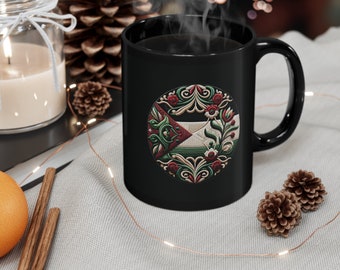 May include: Black coffee mug with a white and green floral design. The design features a circle with a red, white, and green pattern inside.