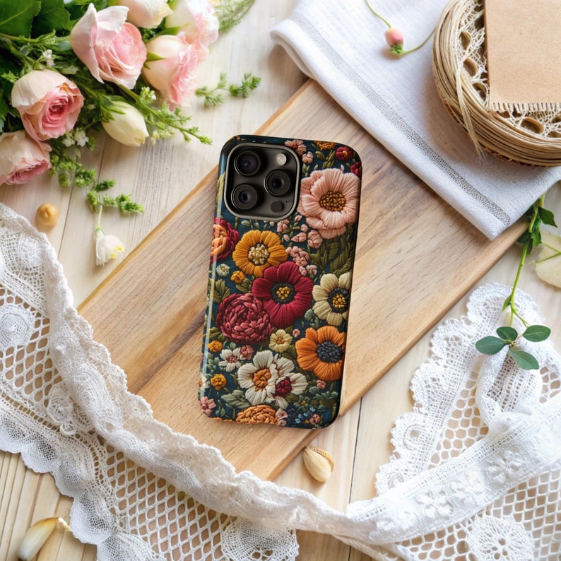 Puede incluir: Una funda para tel&eacute;fono con un dise&ntilde;o floral. La funda es de color azul oscuro con flores bordadas en tonos rojos, naranjas, amarillos y blancos.