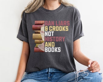 Puede incluir: Una camiseta gris oscuro con un gráfico de estilo vintage que presenta un retrato de Ruth Bader Ginsburg y el texto "Ban Liars & Crooks Not History And Books".