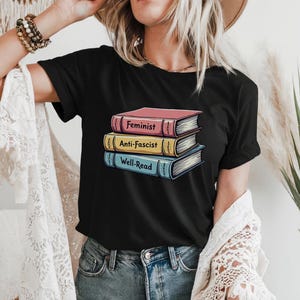May include: Black t-shirt with a graphic of a stack of books. The books have the words "Feminist", "Anti-Fascist", and "Well-Read" on their spines.