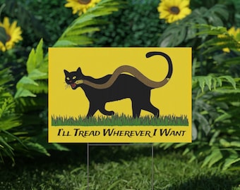 May include: A yellow yard sign with a black cat with a snake wrapped around its body. The cat is looking to the left and has its mouth open. The text on the sign reads "I'll Tread Wherever I Want".