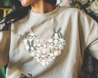 May include: A light beige sweatshirt with a graphic print of a group of bunnies wearing glasses. The bunnies are arranged in a heart shape.