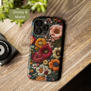 Puede incluir: Una funda para tel&eacute;fono floral con fondo azul oscuro y flores bordadas de colores. La funda tiene un acabado brillante y mate. La funda tiene un recorte para la c&aacute;mara con tres lentes.