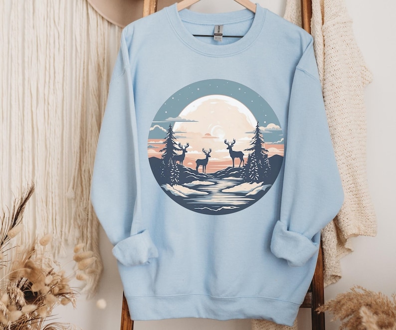 May include: Light blue sweatshirt with a graphic of three deer silhouetted against a full moon and a forest scene.