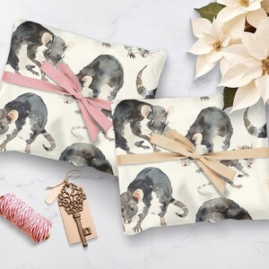K&ouml;nnte beinhalten: Zwei Geschenkboxen, die in wei&szlig;es Papier mit einem Aquarellmuster von schwarzen Ratten eingewickelt sind. Eine Box ist mit einem rosa Band und die andere mit einem braunen Band gebunden.