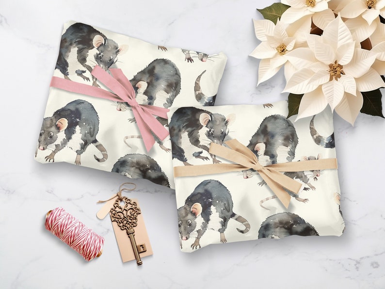K&ouml;nnte beinhalten: Zwei Geschenkboxen, die in wei&szlig;es Papier mit einem Aquarellmuster von schwarzen Ratten eingewickelt sind. Eine Box ist mit einem rosa Band und die andere mit einem braunen Band gebunden.