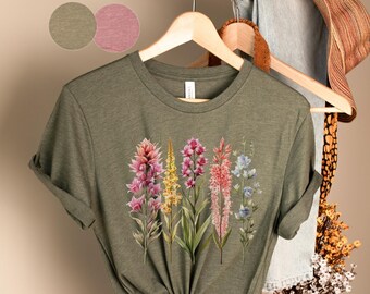 May include: A green t-shirt with a floral print featuring a variety of colorful flowers, including pink, yellow, and blue.