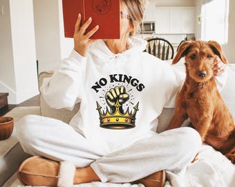 Pode incluir: Moletom branco com um gráfico de um punho quebrando uma coroa dourada e o texto "NO KINGS".