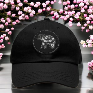May include: Black baseball cap featuring a white floral bear design with the word "mama" on the front.