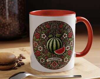 May include: White ceramic mug with a red rim and handle. The mug features a circular design with a watermelon and floral pattern. The design includes the word "PALESTINE" in a banner.