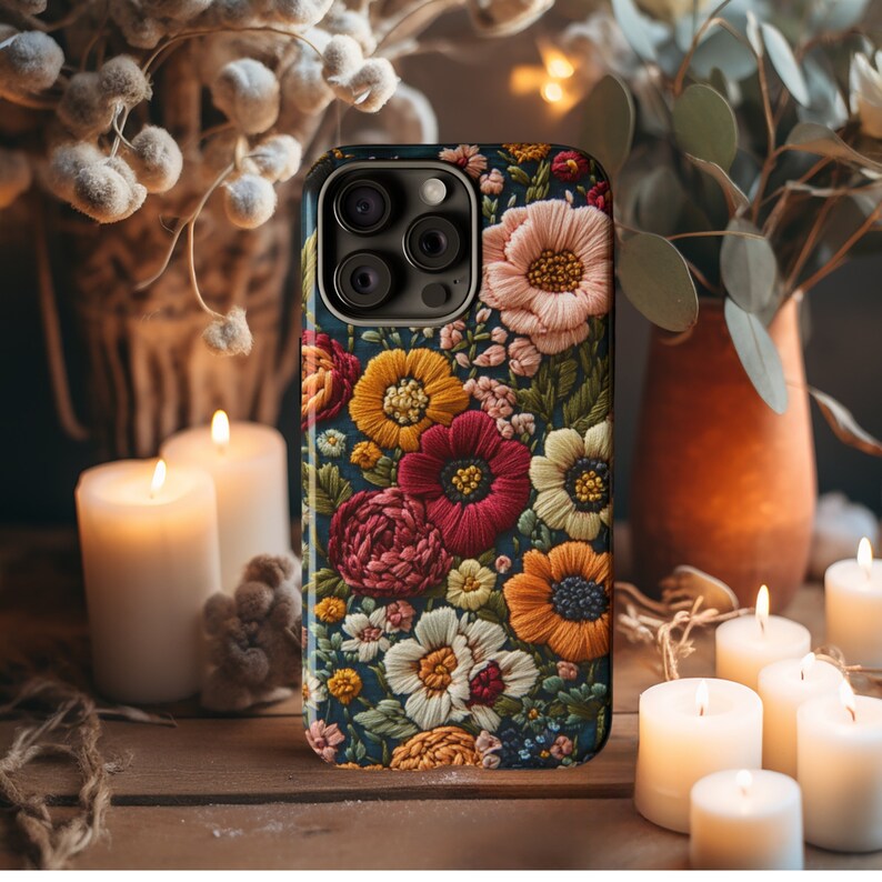 Puede incluir: Una funda para tel&eacute;fono con un dise&ntilde;o floral. La funda es negra con una variedad de flores coloridas bordadas en ella. Las flores son en tonos de rojo, amarillo, naranja y blanco.