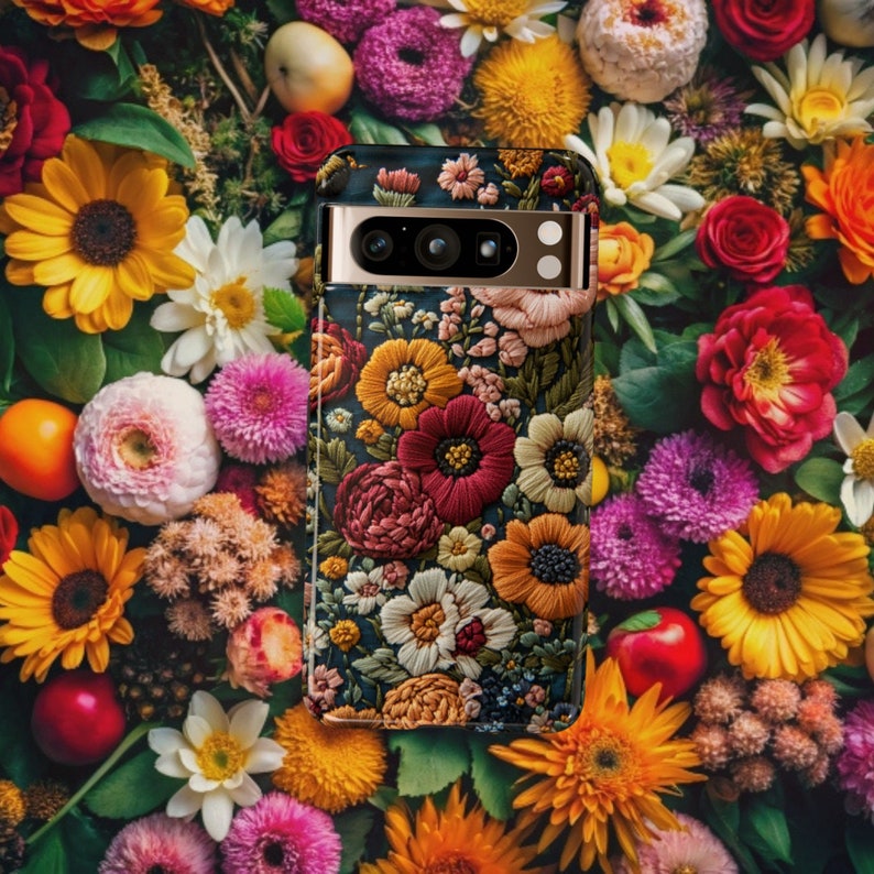 Puede incluir: Una funda de tel&eacute;fono dorada con un dise&ntilde;o de bordado floral. La funda tiene un fondo negro y presenta una variedad de flores de colores, incluyendo rojas, rosas, amarillas y blancas.