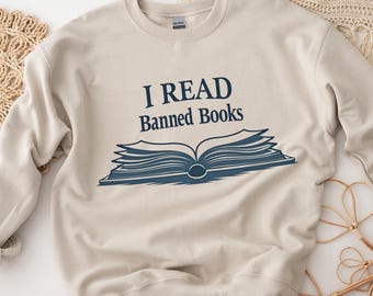 May include: A beige sweatshirt with the text "I READ Banned Books" and a blue illustration of an open book.