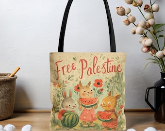 May include: Beige tote bag with black handles featuring the text "Free Palestine" in red script. The bag's design includes illustrations of three cartoon rabbits holding watermelon slices and a whole watermelon, surrounded by flowers and foliage.