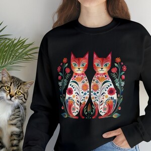 May include: Black sweatshirt with a colorful illustration of two cats with floral patterns. The cats are facing each other and have red, orange, yellow, green, and blue colors.
