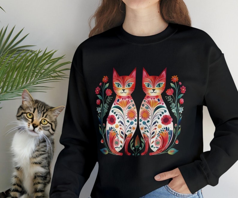 May include: Black sweatshirt with a colorful illustration of two cats with floral patterns. The cats are facing each other and have red, orange, yellow, green, and blue colors.