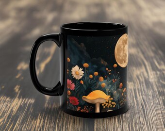 May include: Black ceramic mug featuring a design of a mushroom, flowers, and a full moon against a dark blue starry sky.