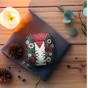 Op de afbeelding: Een witte, rode en groene telefoonhoes met een bloemenpatroon. De hoes heeft een gestileerd bloemenpatroon met rode, witte en groene bloemen.