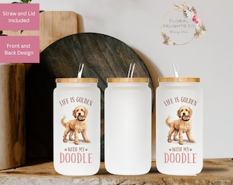 May include: Three frosted glass tumblers with bamboo lids and straws. Two tumblers feature a golden doodle illustration and the text "LIFE IS GOLDEN WITH MY DOODLE". The tumblers are displayed on a wooden shelf.