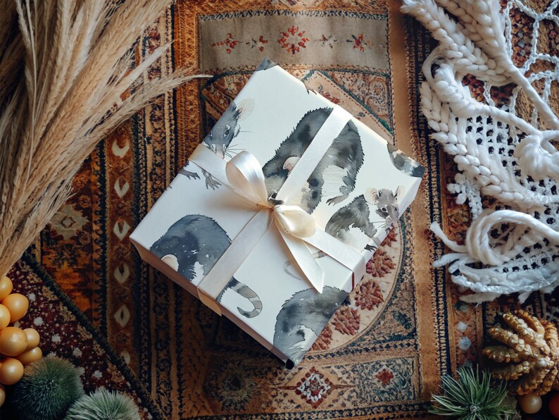 K&ouml;nnte beinhalten: Wei&szlig;e Geschenkpapier mit einem Aquarell-Design aus schwarzen und wei&szlig;en M&auml;usen. Das Geschenkpapier ist mit einem wei&szlig;en Satinband gebunden.