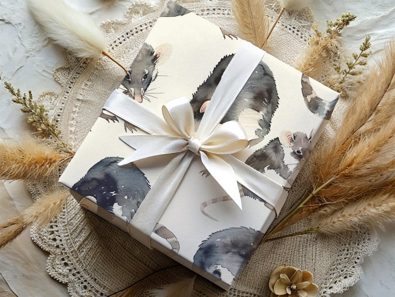 K&ouml;nnte beinhalten: Wei&szlig;e Geschenkpapier mit einem Aquarell-Design von schwarzen und grauen M&auml;usen. Das Geschenkpapier ist mit einem wei&szlig;en Satinband gebunden.