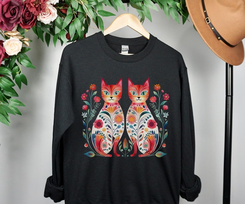 May include: Black sweatshirt with a colorful illustration of two cats with floral patterns. The cats are facing each other and have red, orange, yellow, green, and blue colors.