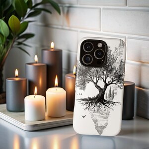 May include: A white phone case featuring a black and white tree design. The case is next to several lit candles in varying shades of gray and white. The candles are on a wooden tray.